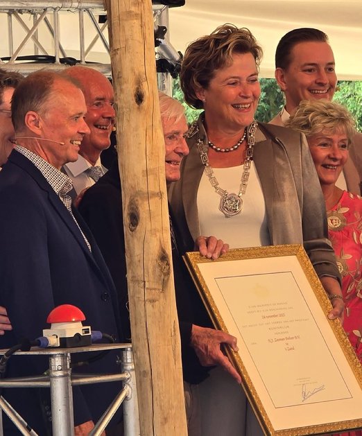 The image depicts a group of people gathered around a table, with a woman holding a framed certificate in the foreground, and a decorative tree in the background.
Door AI gegenereerde inhoud is mogelijk onjuist.