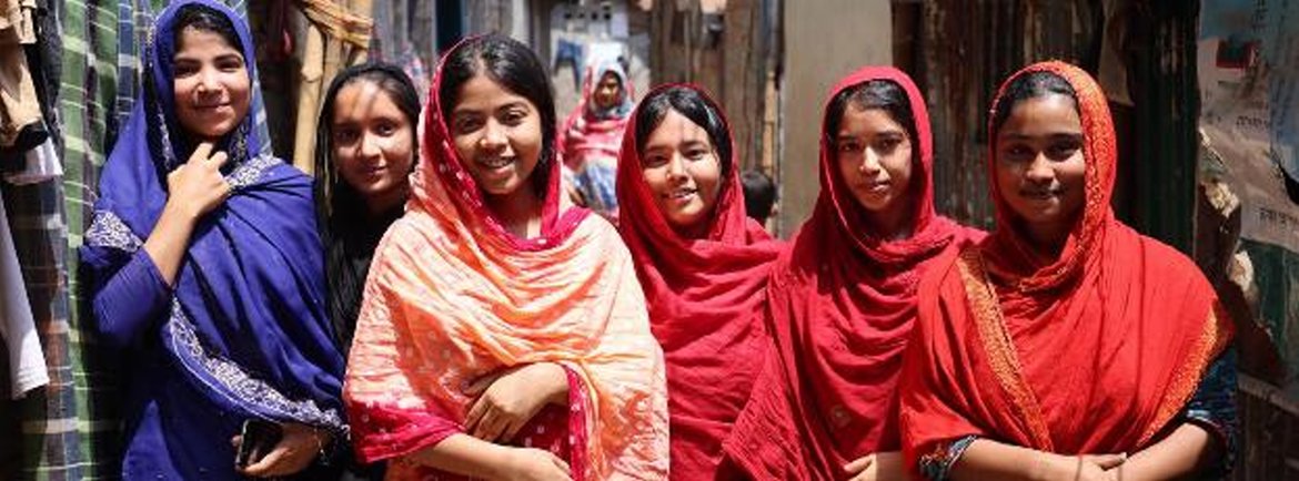 Smiling Bangladeshi girls in traditional clothing stand in a narrow alley