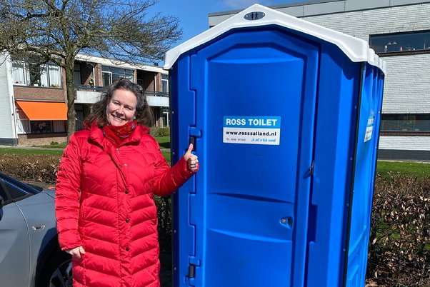 A person standing next to a blue portable toilet

Description automatically generated
