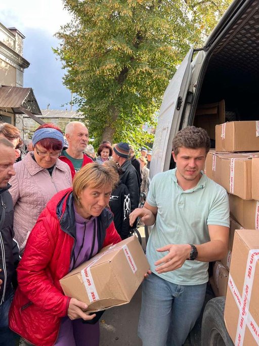 A group of people standing next to a van with boxes

Description automatically generated