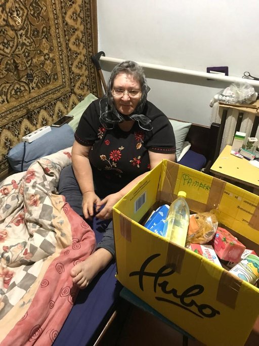 A person sitting on a bed with a box full of food

Description automatically generated